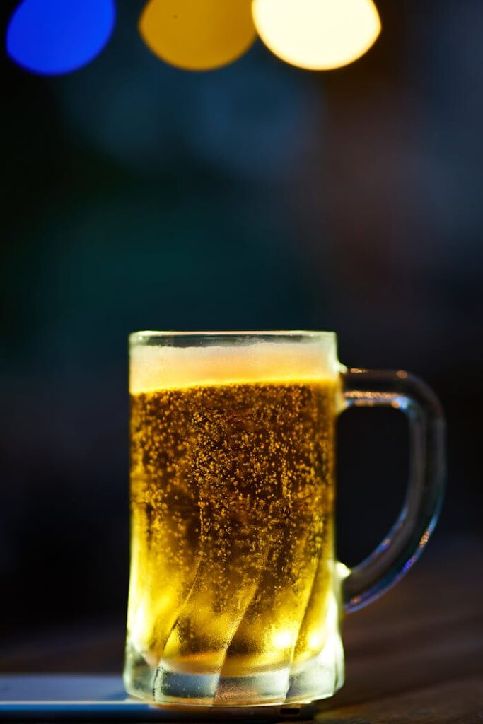 pexels-photo-1672304 A glass mug of cold beer with frothy head and bokeh lighting effect in a dim setting.
